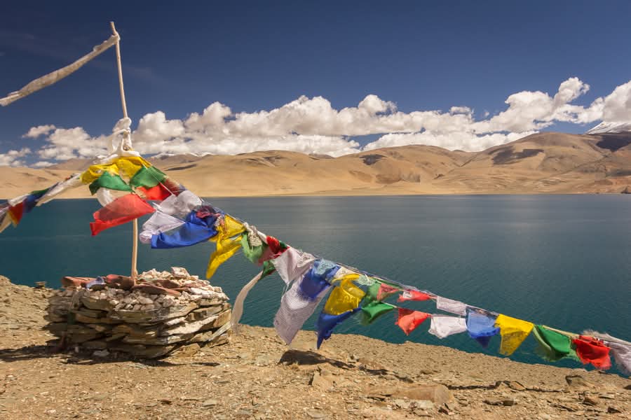 Drapeaux de prières tibétains devant un lac sacré aux eaux turquoise au Ladakh