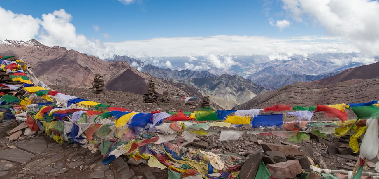 Drapeaux de prières multicolores au sommet d'un col himalayen avec vue panoramique sur les montagnes du Ladakh